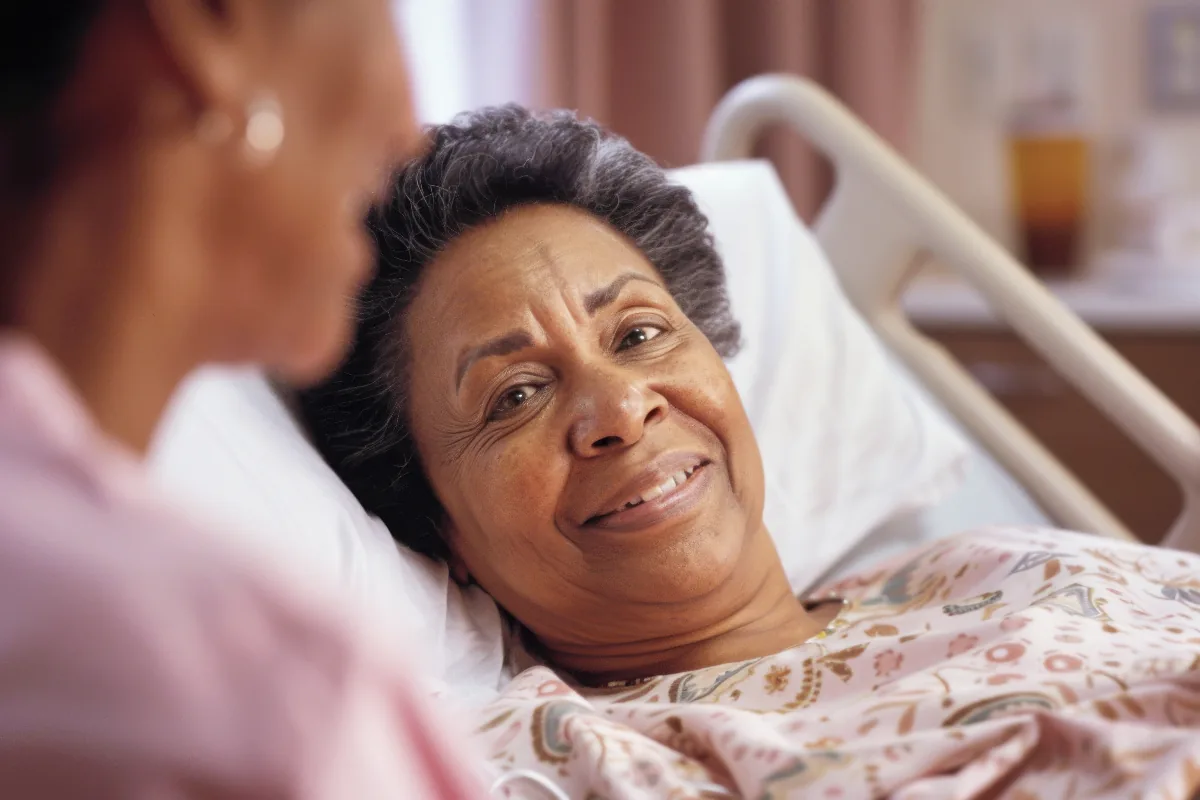 Mujer en una cama hospitalaria conversando con una persona a su lado.