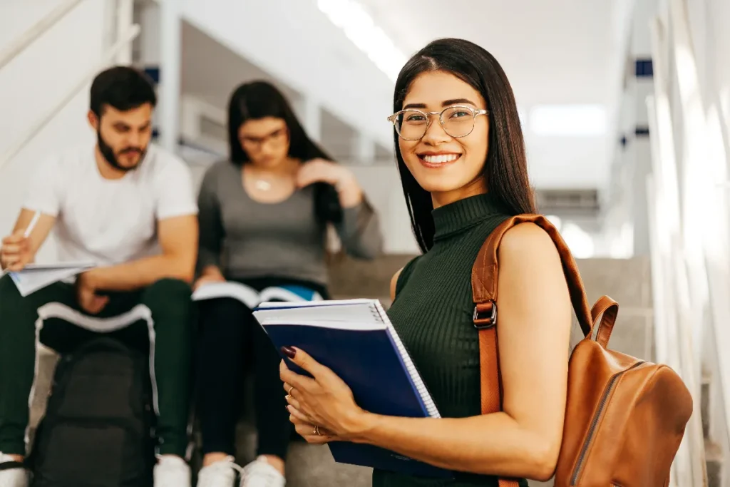 Estudiante con libros y cuadernos en un espacio universitario.